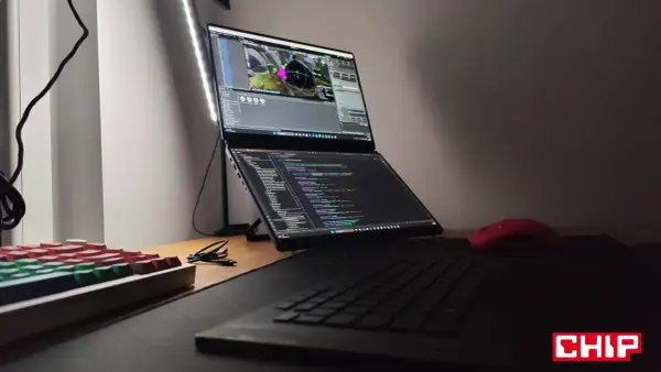 Na biurku laptop z dwoma ekranami, na górnym widać scenę w Unreal Engine 6, na dolnym kod. Obok klawiatura i czerwona myszka.