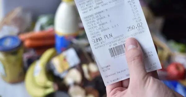 Ręka trzyma paragon z zakupów spożywczych, na którym widnieje suma 250,02 zł. Zastanawiasz się, gdzie wyrzucać paragony? Ten jest z papieru termicznego.