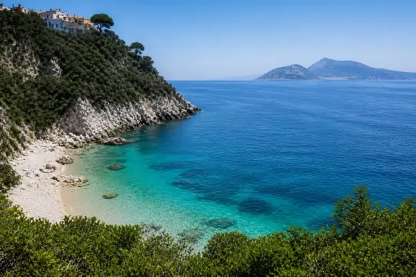 Vue d'une crique aux eaux turquoise cristallines, avec une colline verdoyante et des maisons blanches perchées, près d'une île à côté de Capri.