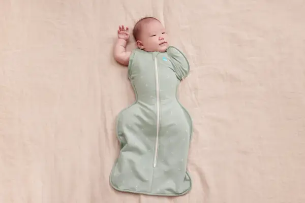 Un neonato dorme sereno, avvolto in una fascia che lo culla dolcemente.