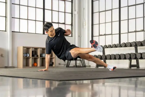 Un homme en tenue de sport exécute un exercice de planche latérale dans une salle de sport.