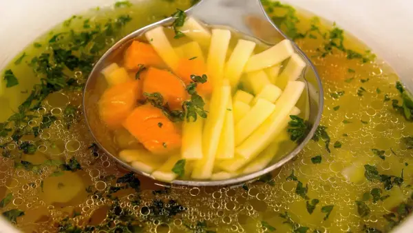 Łyżka nabiera aromatyczny bulion warzywny z marchewką i makaronem nitki.