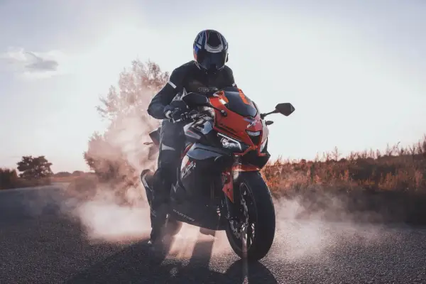 Motocyklista w kasku i kombinezonie na sportowym motocyklu, otoczony dymem. Czy motorem można jeździć po autostradzie? Tak, jeśli spełnia określone wymogi.