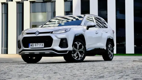Biały Suzuki Across z czarnymi detalami stoi przed nowoczesnym budynkiem.