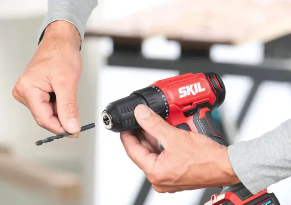 Man insertando una broca en un taladro inalámbrico rojo de la marca SKIL.