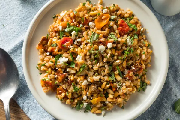 Ensalada de farro que es un plato mediterráneo con tomates secos, piñones y queso feta desmenuzado, todo mezclado con granos de farro.