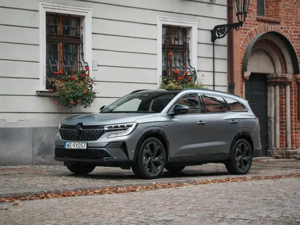 Nowy Renault Espace 2024 w szarym kolorze na brukowanej uliczce, z kwiatami w oknach.