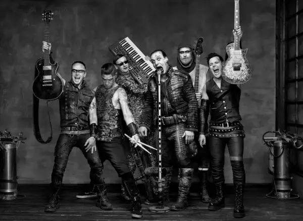 Zespół Rammstein, w tym Till Lindemann, gotowy do rockowego występu. W tle klawisze i gitary, jak w ich hicie "Radio".