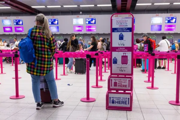 Kolejka do odprawy Wizzair. Tablica informuje, co trzeba wyjąć z bagażu podręcznego: płyny, elektronikę i przedmioty ostre.