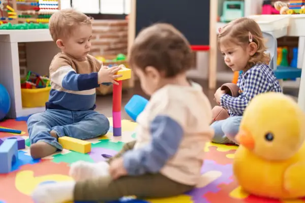 Trójka małych dzieci bawi się klockami i zabawkami na kolorowej macie w żłobku.