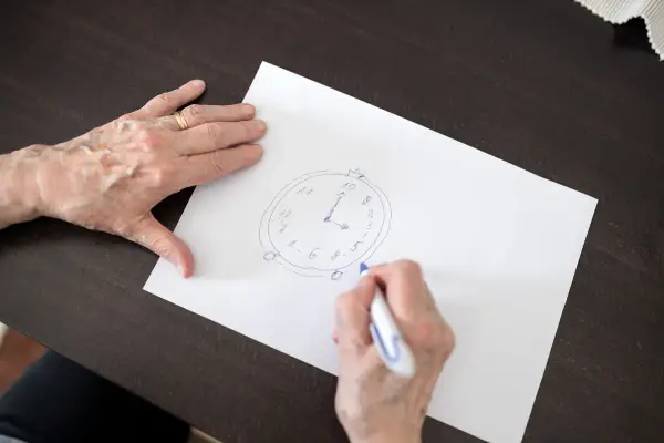 Mani anziane disegnano un orologio su carta, parte di un test memoria anziani.