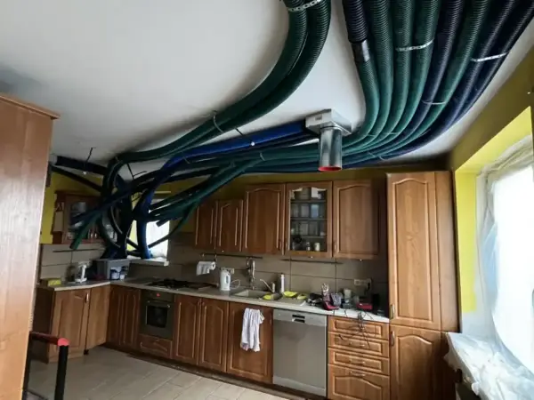 W kuchni starego domu instalacja rekuperacji tworzy gęstą sieć zielonych i niebieskich rur na suficie, przypominając futurystyczny system wentylacyjny.