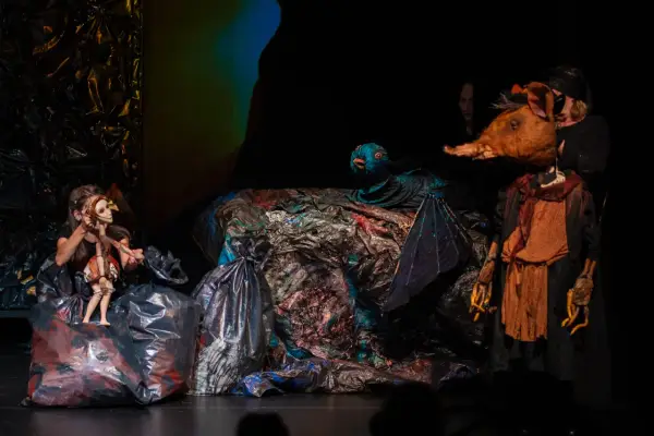 Na scenie teatru lalki i aktora w Łomży, dziewczynka animuje drewnianą lalkę, obok niej ptak i postać z głową zwierzęcia.