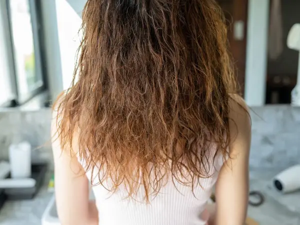 Wilgotne, brązowe włosy z widocznym **frizz** opadają na ramiona.
