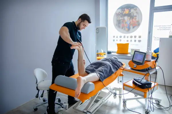 Fizjoterapeuta wykonuje zabieg falą uderzeniową na stopę pacjenta.