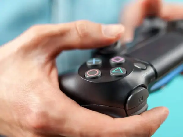 Manos sujetando un mando de PS4, con enfoque en los botones.