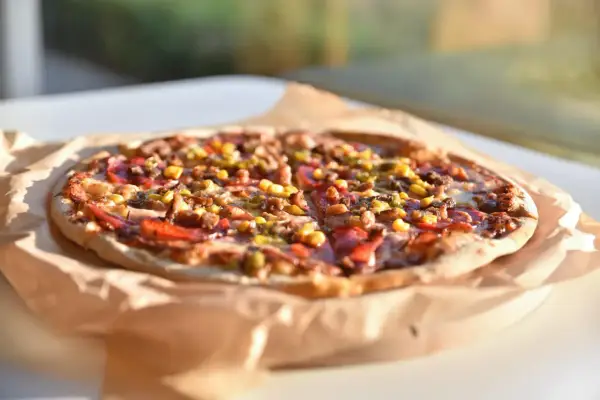Apetyczna pizza Giuseppe 4 sery, z kukurydzą i mięsem, na papierze do pieczenia, w słonecznym świetle.