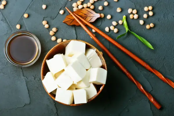 Kostki tofu, czyli przetworzona fasola sojowa, w drewnianej misce, obok sosu sojowego i pałeczek.