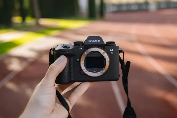Dłoń trzyma aparat Sony Alpha 9 z obiektywem. Jego zaawansowany **global shutter** pozwala na uchwycenie dynamicznych scen bez zniekształceń.