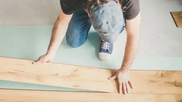 Uomo posa pannelli per come isolare il pavimento dal freddo. Sottile strato isolante azzurro sotto le assi di legno.