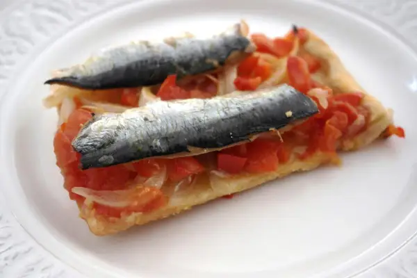 Rebanada de masa con tomate, cebolla y dos sardinas enteras, un plato que recuerda a las sardinas San Juan.