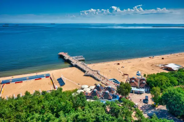 Piękny dzień na plaży w Polsce. Molo wchodzi w głąb morza, a piasek jest pełen ludzi cieszących się wakacjami.