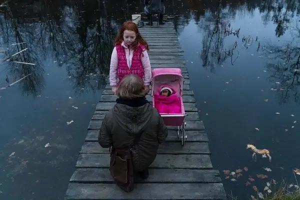 Dwie dziewczynki na drewnianym pomoście, jedna z wózkiem dla lalek, druga obok. Scena jak z filmu "ciemno prawie noc".