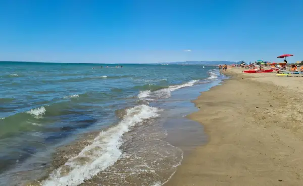 Plage de Fregene, mer bleue, sable doré, parasols et baigneurs profitant du soleil.