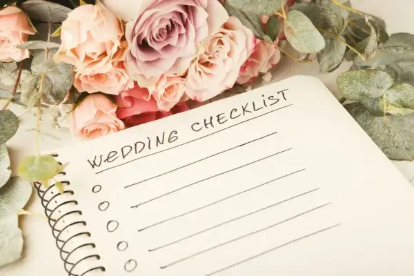 Bukiet róż i eukaliptusa obok notatnika z napisem "Wedding Checklist". Planowanie przebiegu wesela zaczyna się od listy zadań.