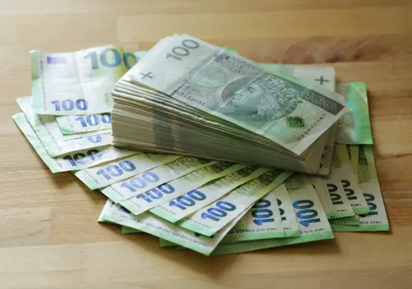 Stos banknotów 100 zł i 100 euro na drewnianym blacie. Może to być kwota na zasiłek stały.