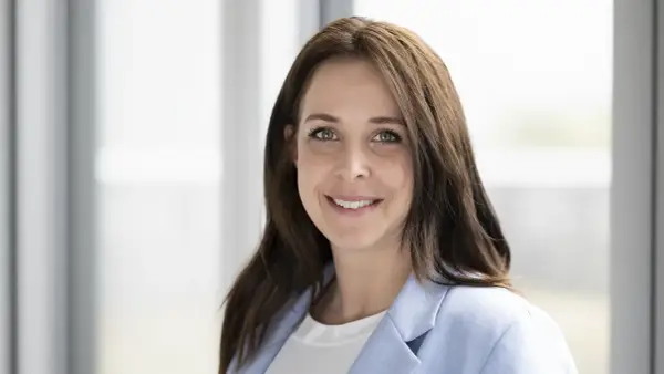 Porträt einer lächelnden Frau mit braunen Haaren und einem hellblauen Blazer. Dies ist eine klare Definition eines Porträts.