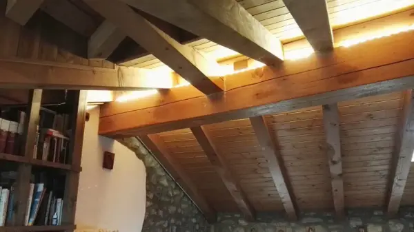 Soffitto in legno con travetti a vista, illuminato da luce naturale. Si nota una libreria e pareti in pietra. La lunghezza massima travetti solaio è ben visibile.