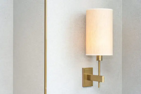Aplique de pared moderno con pantalla de tela beige, montado en una pared con textura gris.
