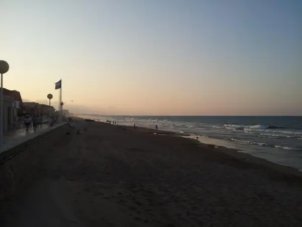 Gente pasea por la **playa de Piles** al atardecer, con el mar y el cielo en tonos pastel.