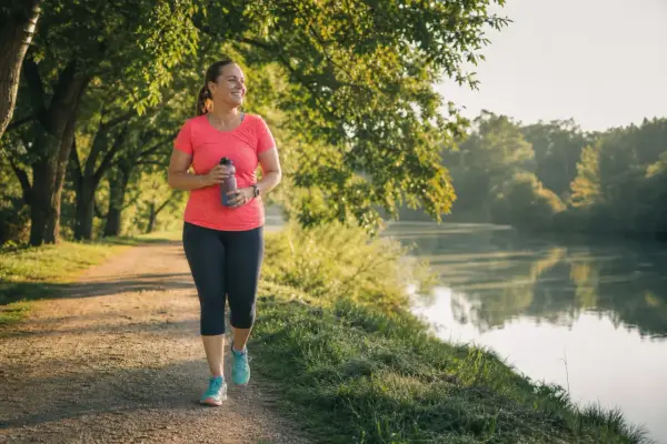 Frau genießt ihr Lauftraining am See. Nach 1 Monat Joggen fühlt sie sich fitter und strahlt Selbstvertrauen aus.