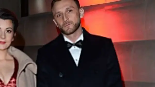 Kamil Nożyński z partnerką na ściance. Elegancki garnitur i czerwona sukienka.