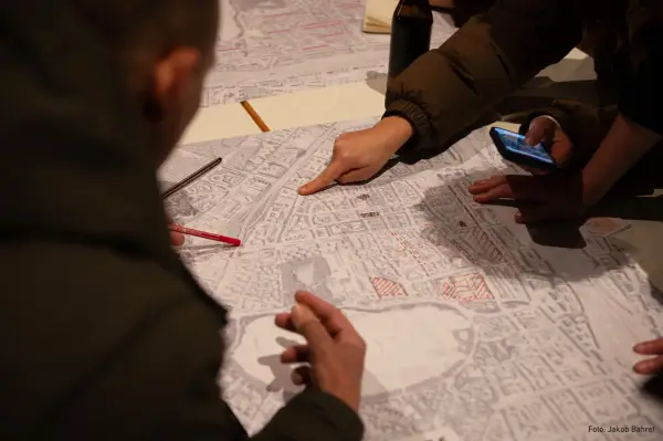 Menschen diskutieren auf einer Karte, die Details der Stadt zeigt. Sie planen die monitoring soziale stadtentwicklung, markieren Bereiche und nutzen ein Smartphone.