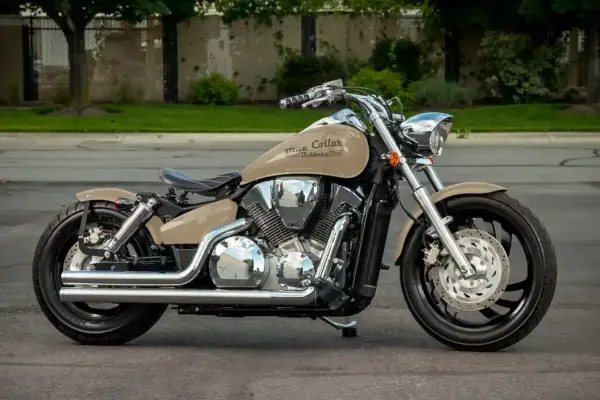 Beżowy motocykl Honda VTX 1300 z chromowanymi elementami i czarnym siedzeniem, zaparkowany na ulicy.
