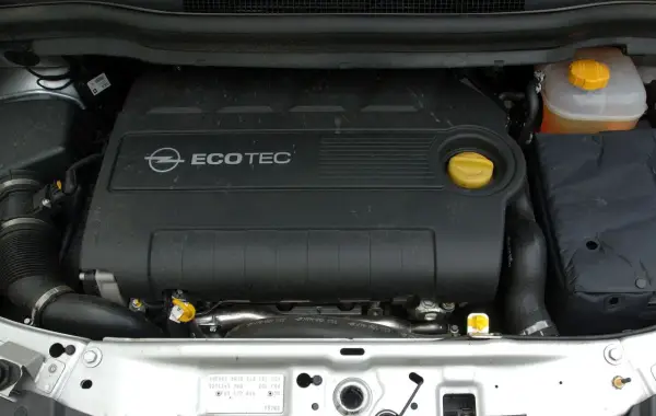 Silnik Ecotec w Oplu Zafira B. Widoczny czarny plastikowy dekiel z logo Opla i napisem Ecotec, żółty korek oleju i zbiorniczek płynu chłodniczego.