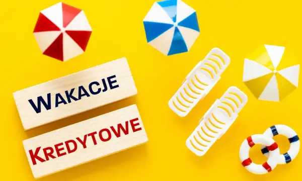 Drewniane klocki z napisem "Wakacje Kredytowe" na żółtym tle, otoczone miniaturowymi parasolkami plażowymi i kołami ratunkowymi.