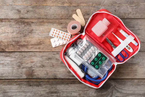 Trousse de secours pharmacie liste : pansements, rouleau de sparadrap, pilules, thermomètre, ciseaux, stéthoscope et masque.