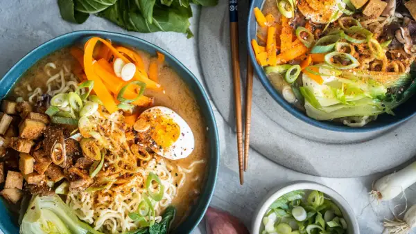 Zwei Schüsseln dampfendes Miso Ramen mit Nudeln, Ei, Karotten, Pak Choi und Frühlingszwiebeln.