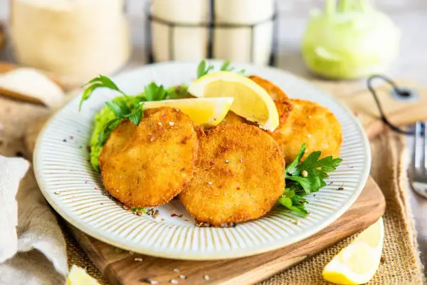 Knusprige Kohlrabi-Schnitzel auf einem Teller mit Erbsenpüree, Zitrone und Petersilie. Ein köstliches vegetarisches Gericht.