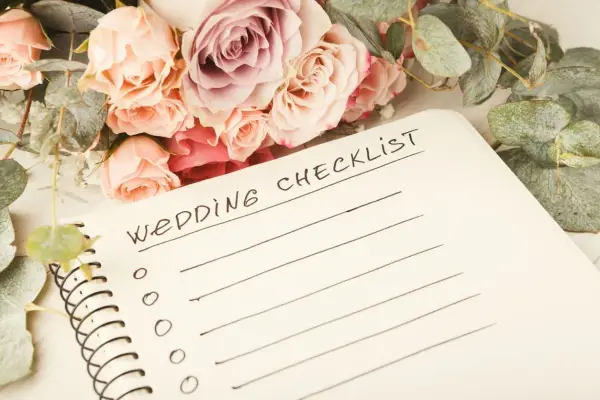 Bukiet róż i eukaliptusa obok notatnika z napisem "Wedding Checklist". Idealna lista spraw do organizacji wesela.