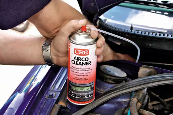 Ręce z zegarkiem trzymają puszkę "Airco Cleaner" do czyszczenia klimatyzacji. Zastanawiasz się, ile kosztuje nabicie klimatyzacji? Ten produkt może pomóc.