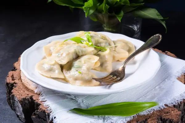 Pyszne pierogi ze szpinakiem i serem, udekorowane czosnkiem niedźwiedzim, na białym talerzu.