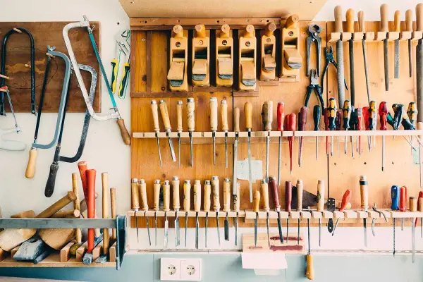 Un bel aménagement atelier avec des rabots, des scies, des tournevis et d'autres outils de menuiserie bien rangés sur un panneau en bois.