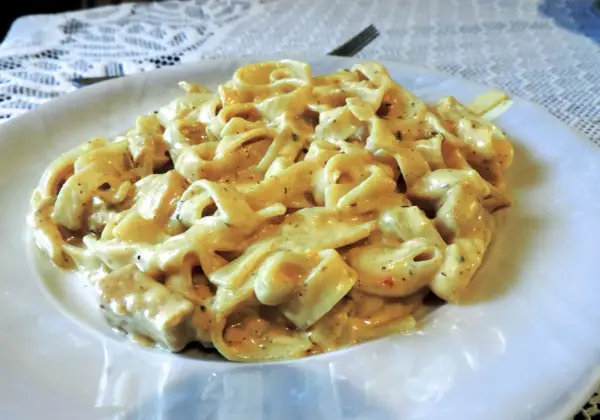 Pyszne makaron tagliatelle z kurczakiem w kremowym sosie, podane na białym talerzu.