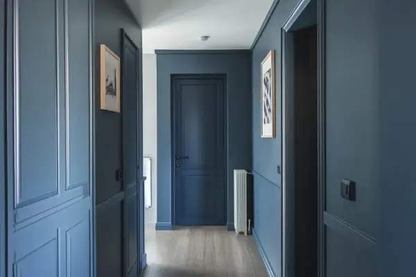 Peinture d'un couloir aux tons bleus profonds, avec des portes assorties et des cadres de portes ornés. Des tableaux discrets ornent les murs.