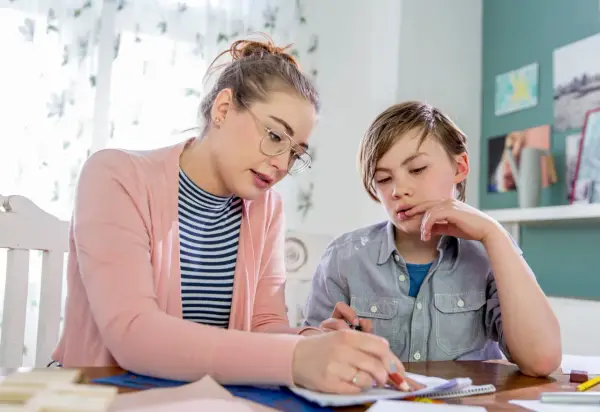 Junge Frau bietet Nachhilfe an. Sie erklärt einem Jungen konzentriert eine Aufgabe auf Papier.